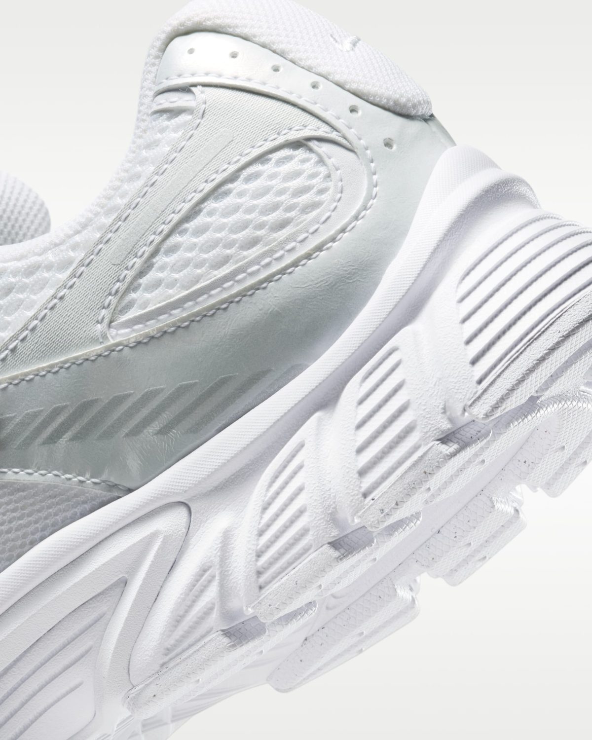 Close-up of a white athletic sneaker focusing on the mesh upper and stitched overlays.