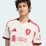 Close-up portrait of a person wearing a white Liverpool FC football jersey with red detailing and crest visible on the chest.