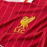 Close-up of a red Liverpool FC jersey featuring yellow pinstripes and the embroidered club crest in gold.