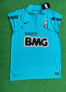 Turquoise soccer jersey laid flat with Banco BMG sponsor logo across the front and a club crest on the chest, on a green surface.