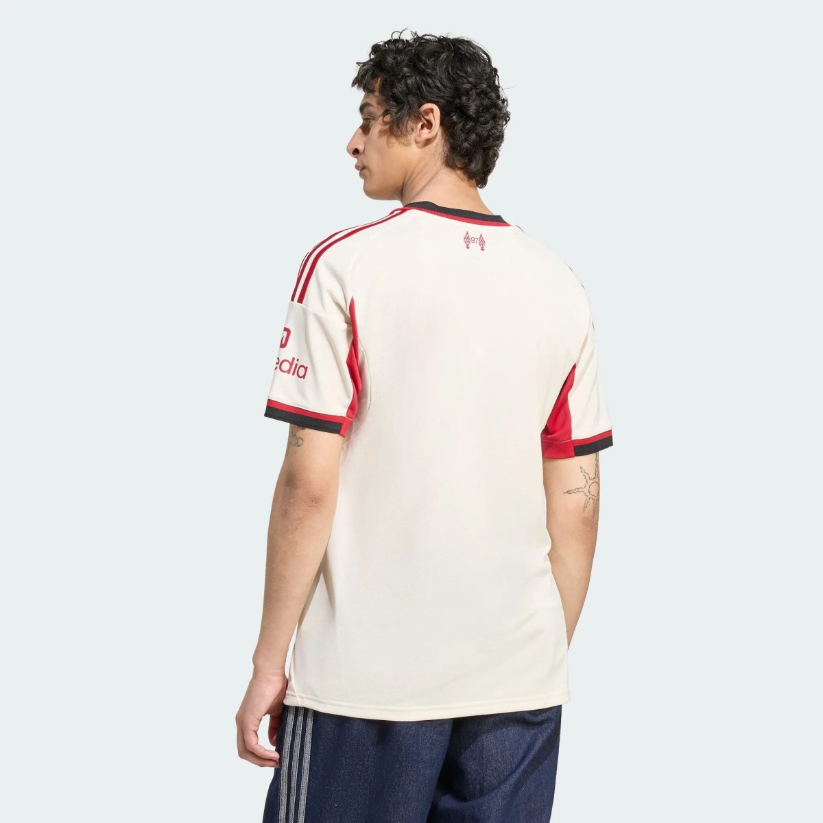 Back/side view of a person wearing a white sports jersey with red trim, against a pale blue background.