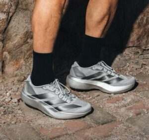 rn-image_picker_lib_temp_54c636a9-41fe-47c0-b0c9-f76483673c08 | UAE SPORT STORE Pair of silver running shoes with white laces on a rocky trail, worn with black socks by a hiker/runner.