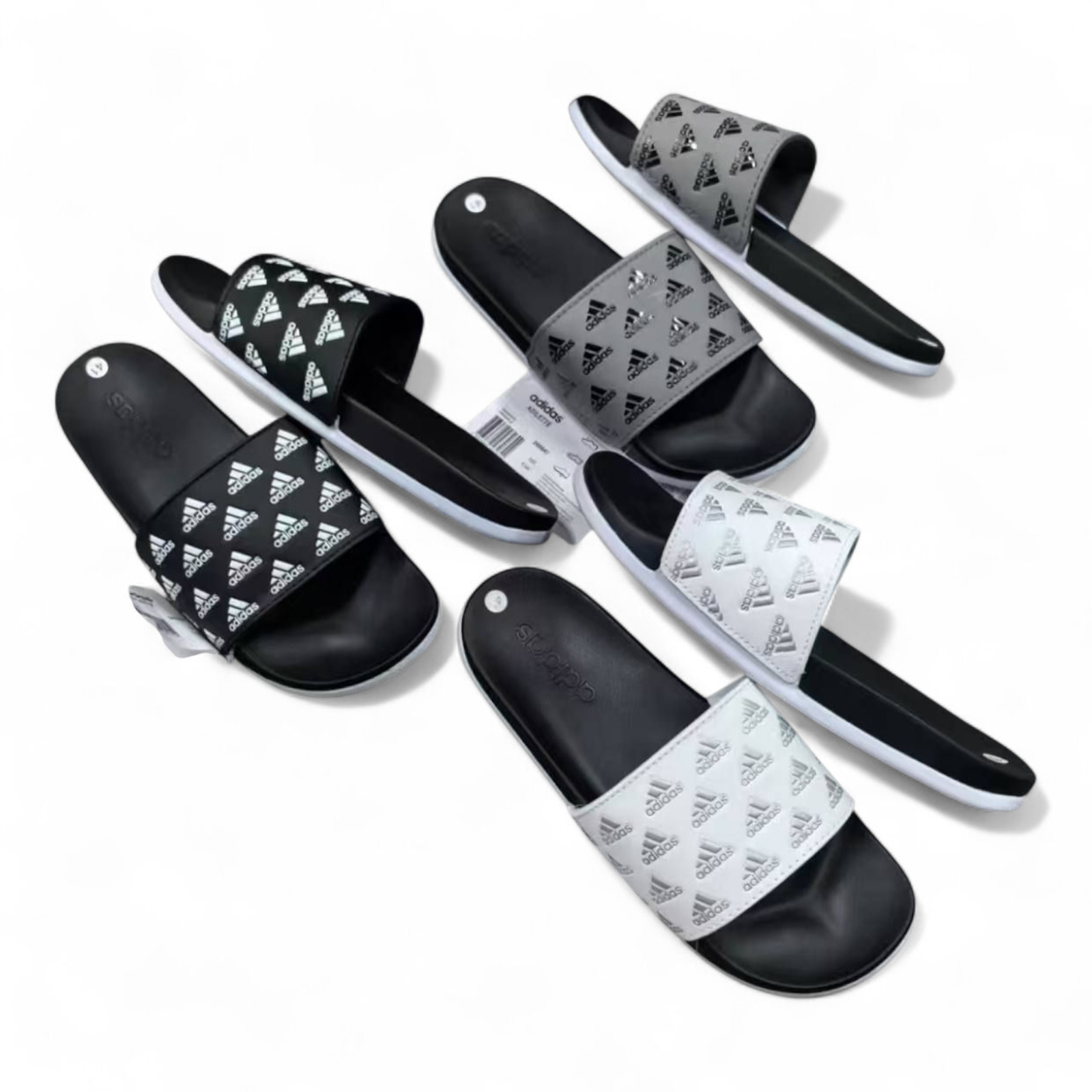 rn-image_picker_lib_temp_565550c2-f346-4c88-a00f-79e0b28baa02 Assorted Adidas slide sandals in black, white, and gray with the brand logo on the straps, laid out on a white background.