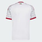 Back view of a white sports jersey with red sleeve cuffs and a small UAE flag near the neckline, light patterned sleeves nearby.