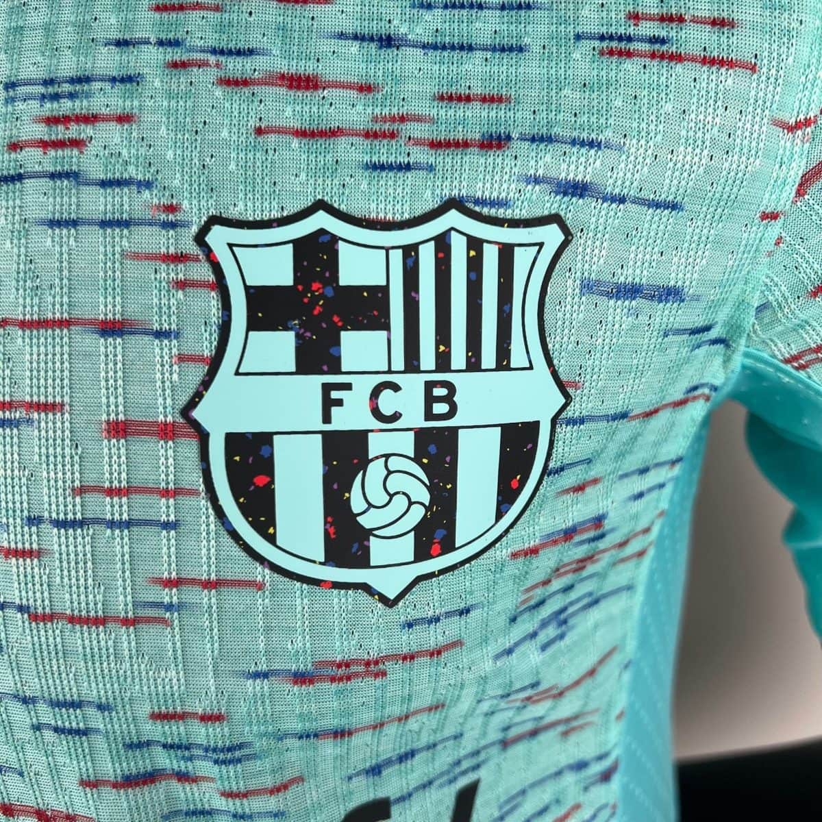 Close-up of a light-blue jersey featuring an FC Barcelona shield logo with colorful confetti specks.