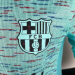 Close-up of a light-blue jersey featuring an FC Barcelona shield logo with colorful confetti specks.
