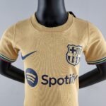 Close-up of a beige sports jersey on a mannequin, showing a blue Nike swoosh and a crest with FCB on the chest, plus striped sleeve edges.