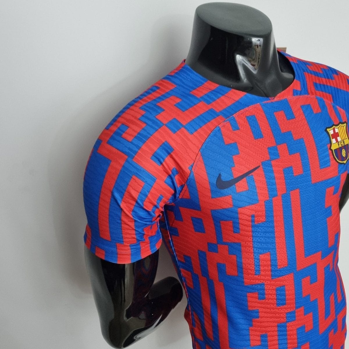 Close-up of a blue and red geometric soccer jersey on a black mannequin, with a small FC Barcelona crest visible on the chest.