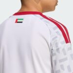 Back of a person wearing a white sports jersey with red trim and a small UAE flag patch on the shoulder area.