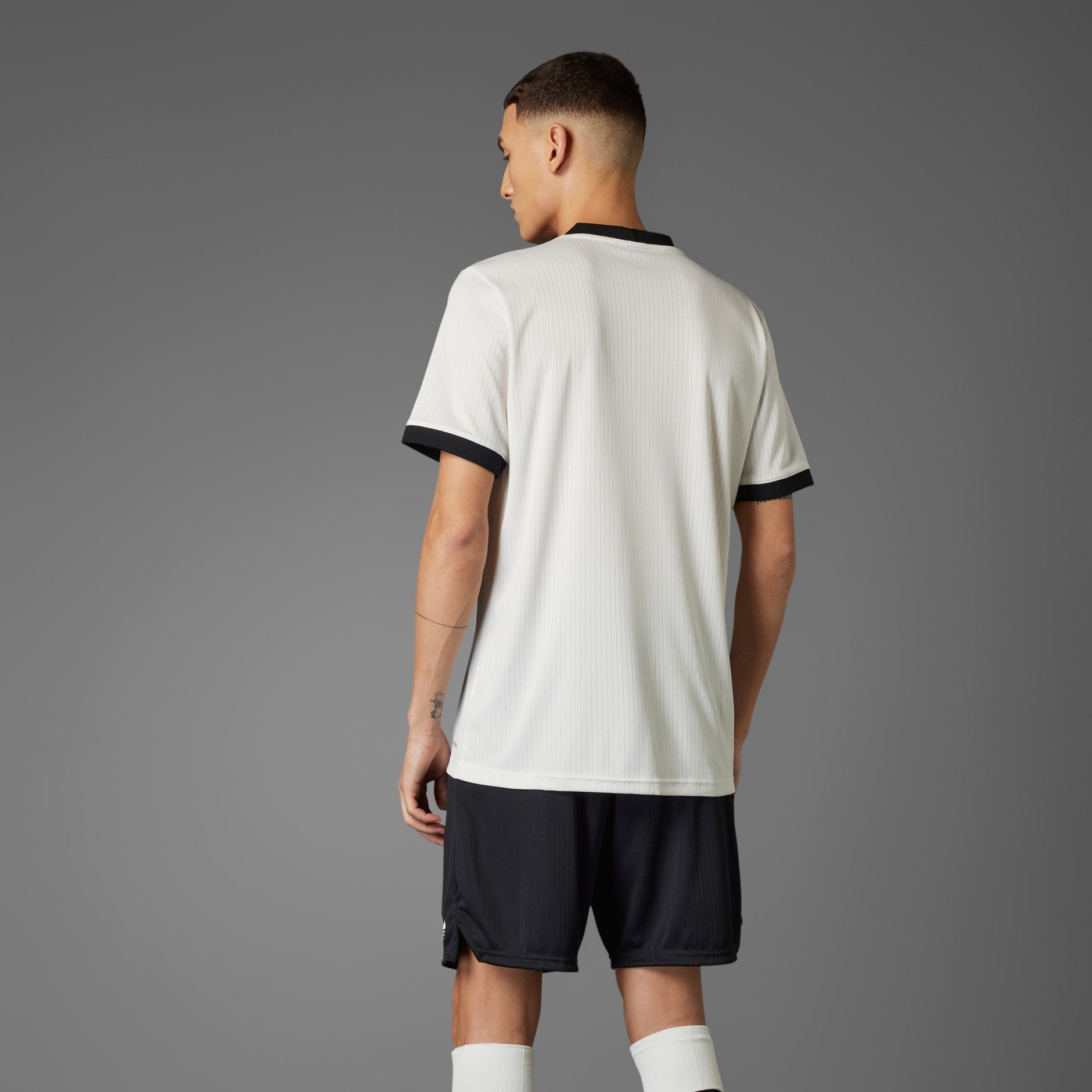 rn-image_picker_lib_temp_5c745790-c83b-4b8f-bf3c-736f49f09d1a | UAE SPORT STORE Back view of a person wearing a white sports jersey with black cuffs against a gray background, seen from behind.