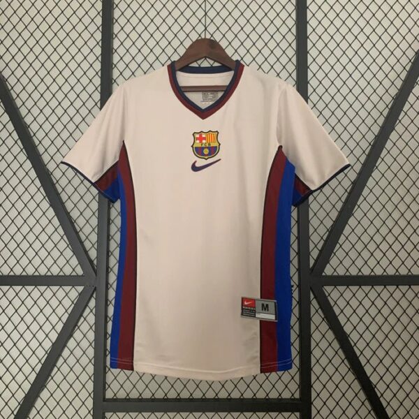 White FC Barcelona soccer jersey on a hanger, with red and blue side panels, Barcelona crest on the chest, and a Nike swoosh.