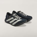 Close-up of black athletic shoes with white stripes against a light background, showing side details and laces.
