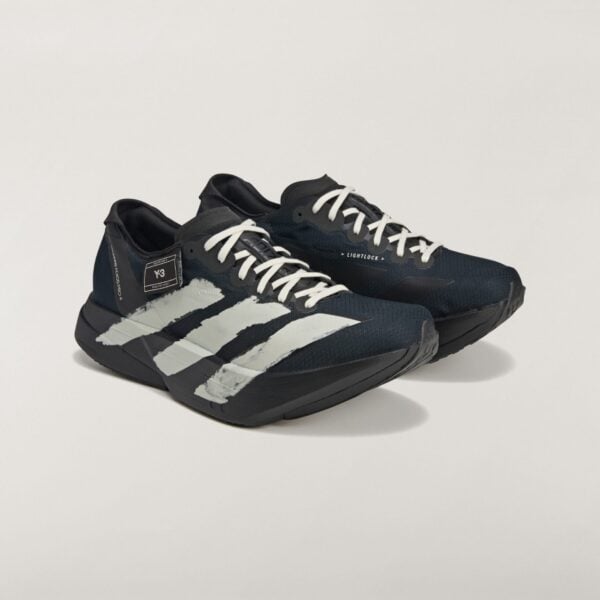 Close-up of black athletic shoes with white stripes against a light background, showing side details and laces.