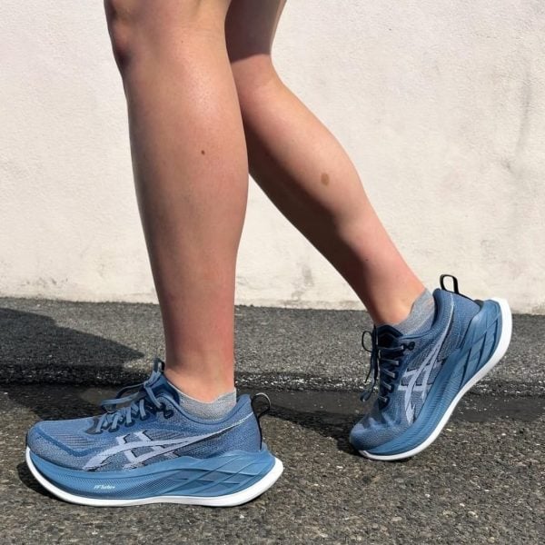 Person mid-step wearing blue running shoes on a pavement surface outdoors, legs visible from knees down(sunny day).