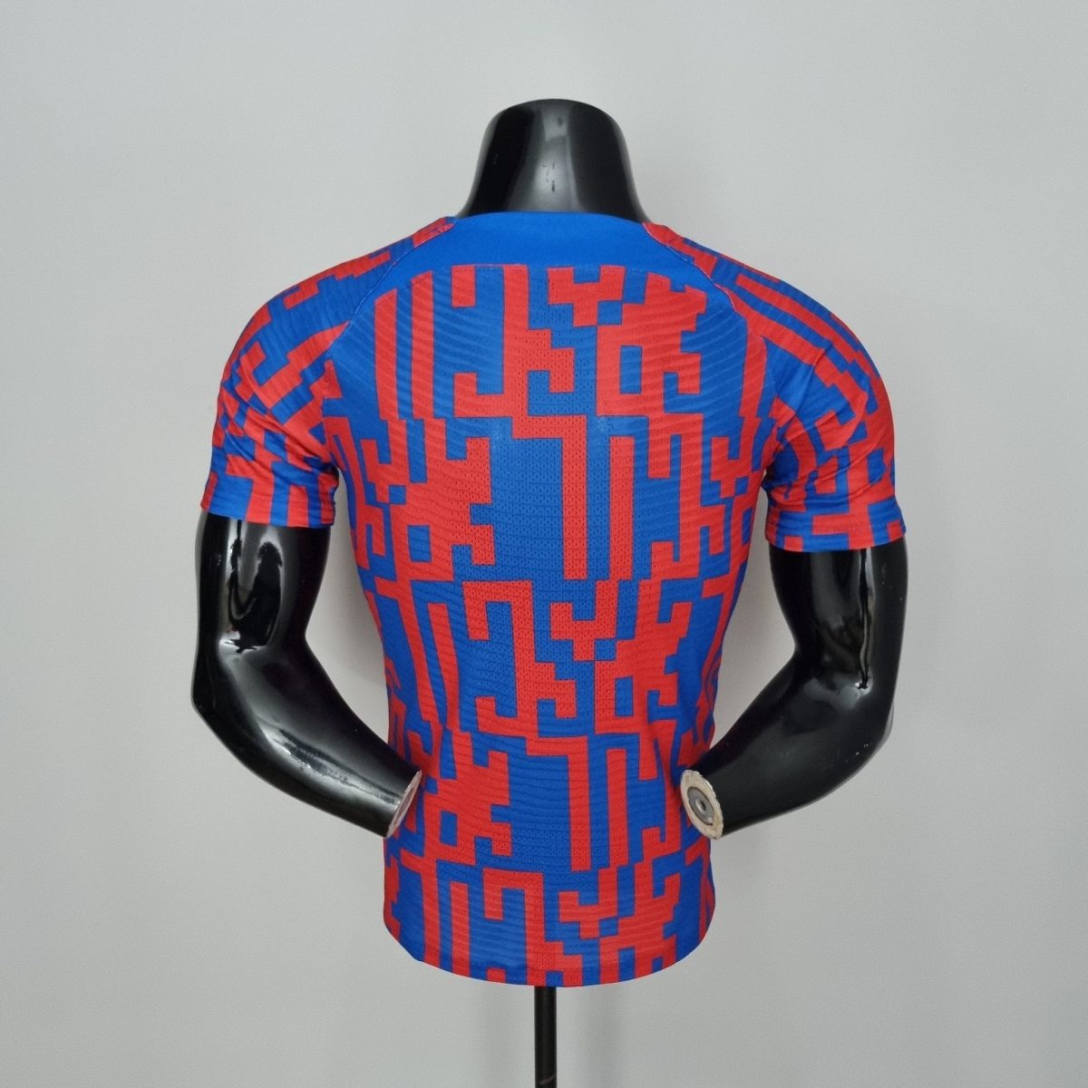 Back view of a blue and red geometric-pattern athletic jersey on a black mannequin torso