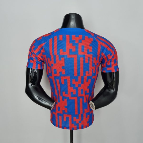 Back view of a blue and red geometric-pattern athletic jersey on a black mannequin torso