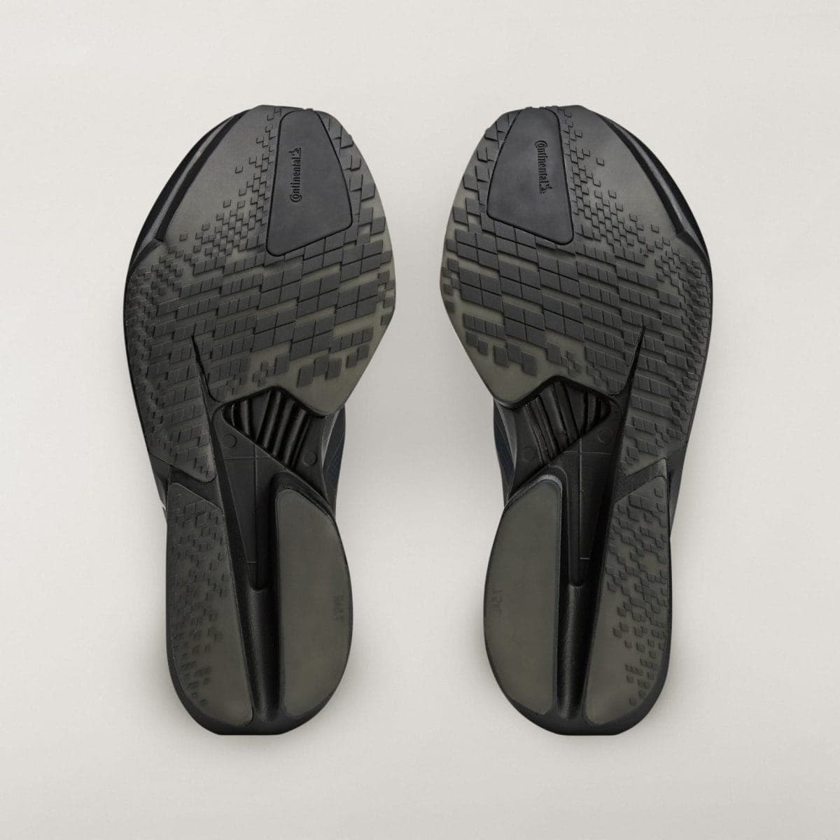 Bottom view of two dark sneakers with textured sole patterns facing upward