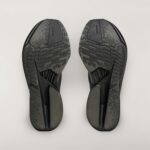Bottom view of two dark sneakers with textured sole patterns facing upward