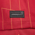 Black fabric patch tag sewn onto red plaid fabric; it reads ENGINEERED with the code 364536AAC2 and a small emblem.