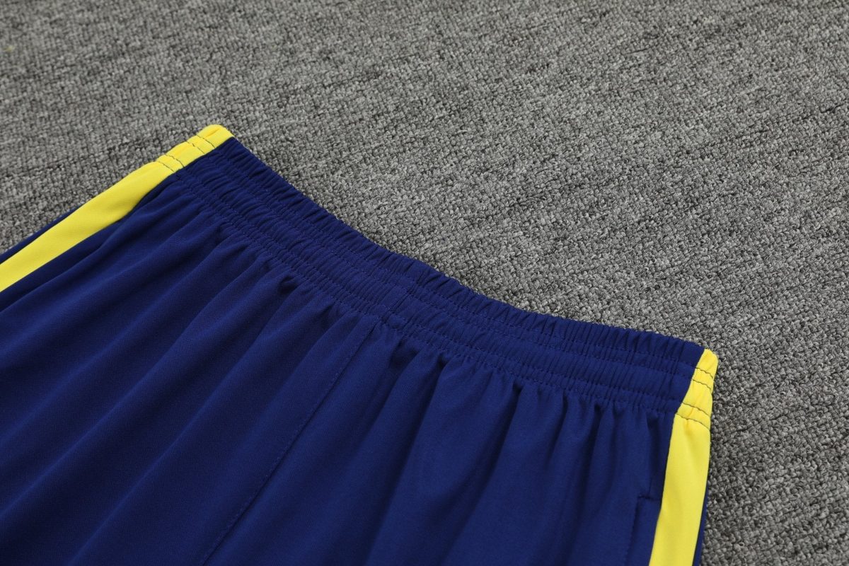 Blue athletic shorts with a yellow stripe along the seam on a gray carpet.
