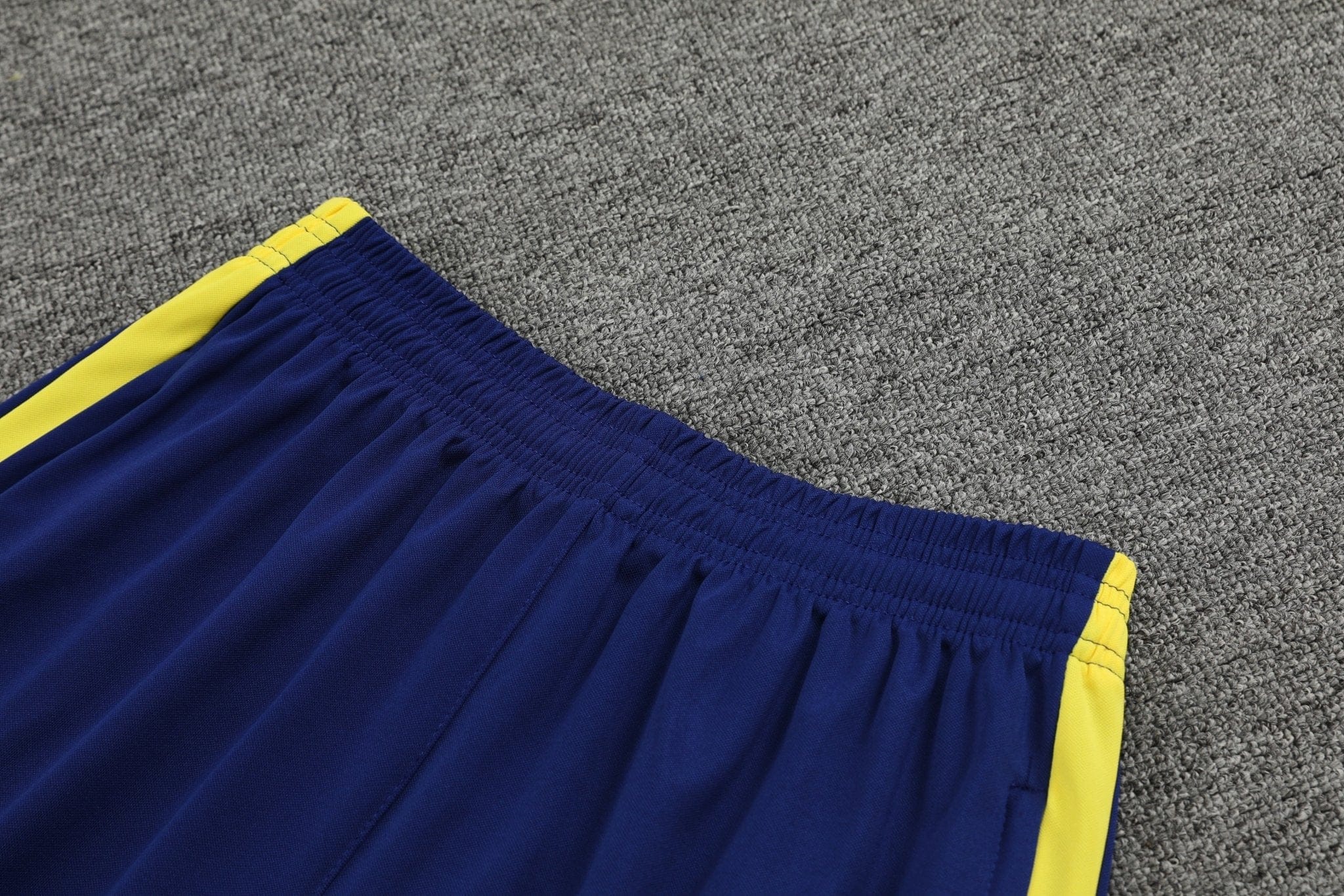 rn-image_picker_lib_temp_6b418879-679a-4da6-8c92-d5aa0b4d0266 | UAE SPORT STORE Blue athletic shorts with a yellow stripe along the seam on a gray carpet.