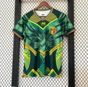 Green football jersey with yellow geometric patterns and an eagle emblem, Mali federation crest on the chest, hanging on a wooden hanger against a mesh background.