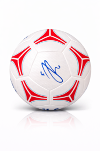 White soccer ball with red and blue geometric panels and a blue autograph in the center.