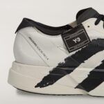 Close-up of a white and black sneaker showing the midsole and textured upper with a black brush-stroke graphic across the shoe.