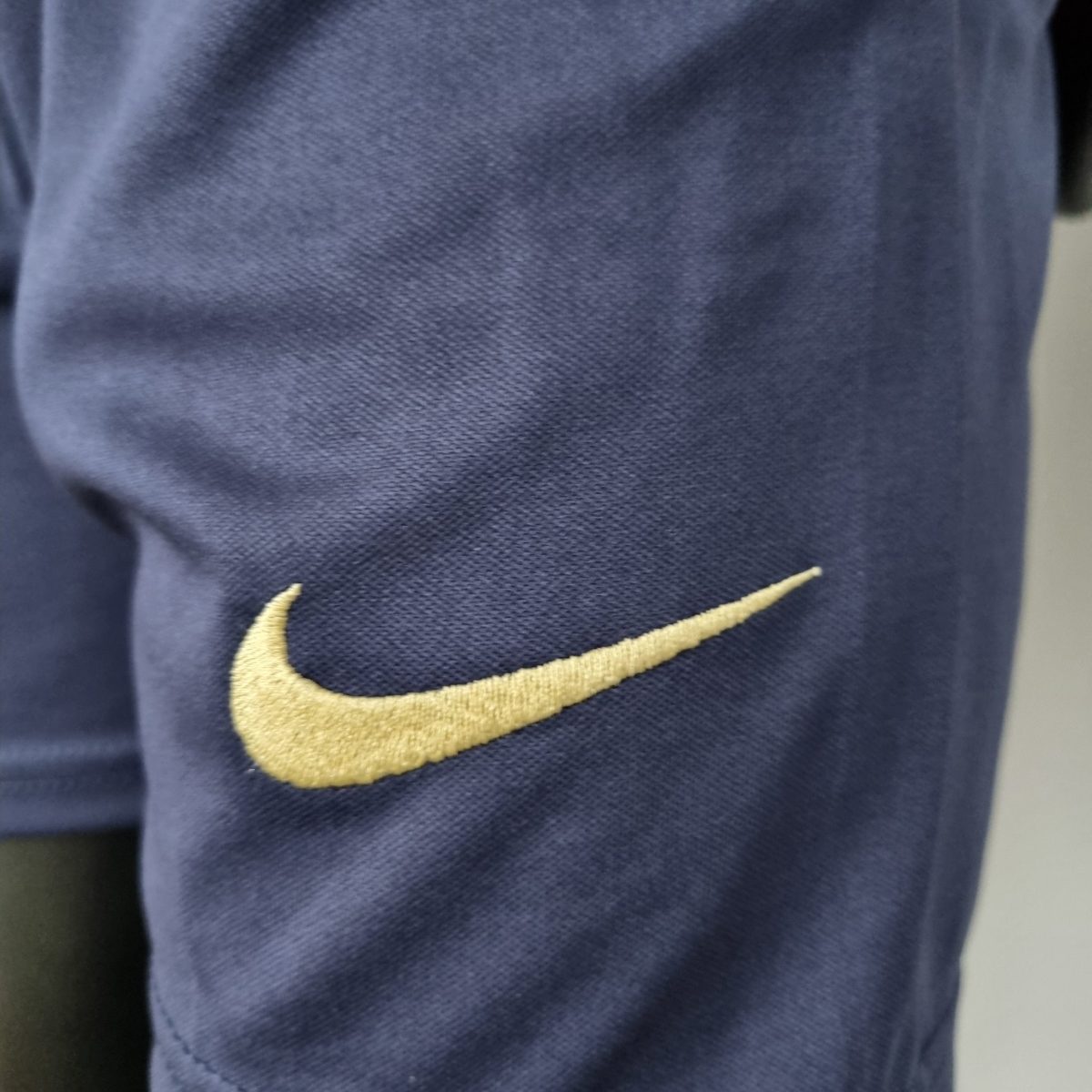 Close-up of dark blue fabric with a gold Nike swoosh logo stitched on it.
