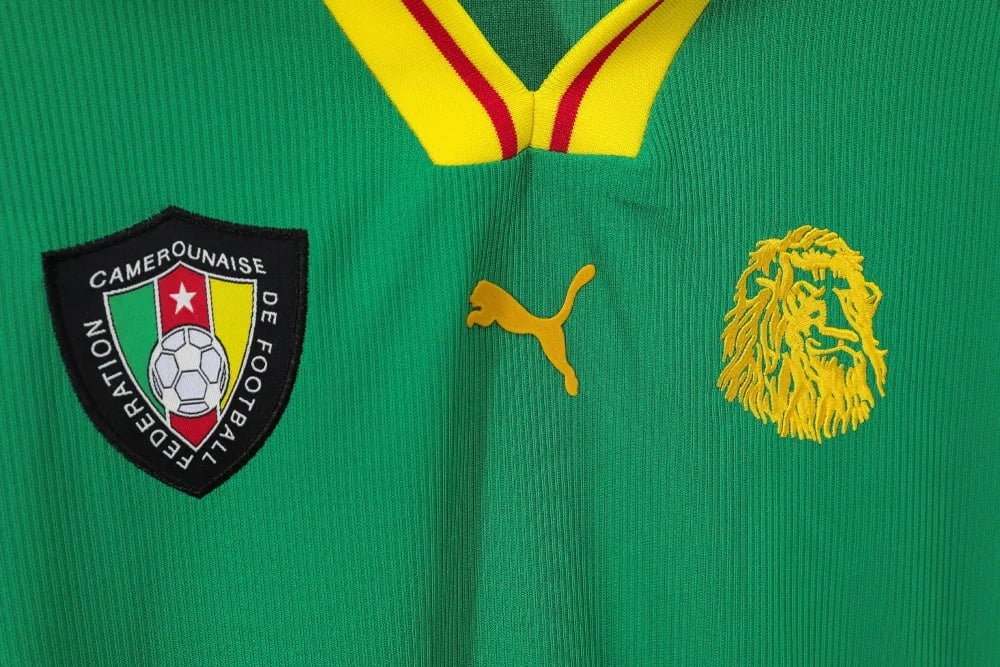 rn-image_picker_lib_temp_7e659a89-a99c-4aa2-9359-b7c5b68dd88c | UAE SPORT STORE Cameroon national football team jersey with crest, Puma logo, and gold lion emblem on green fabric with yellow-red collar accents