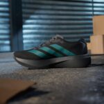 Close-up of a black athletic shoe with turquoise stripes resting on a concrete floor, blurred blue metal doors in the background.