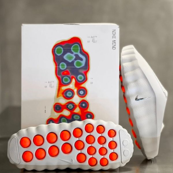 White Nike running shoe with bright orange circular outsole pods; box behind shows a multicolored foot-pressure heat map.