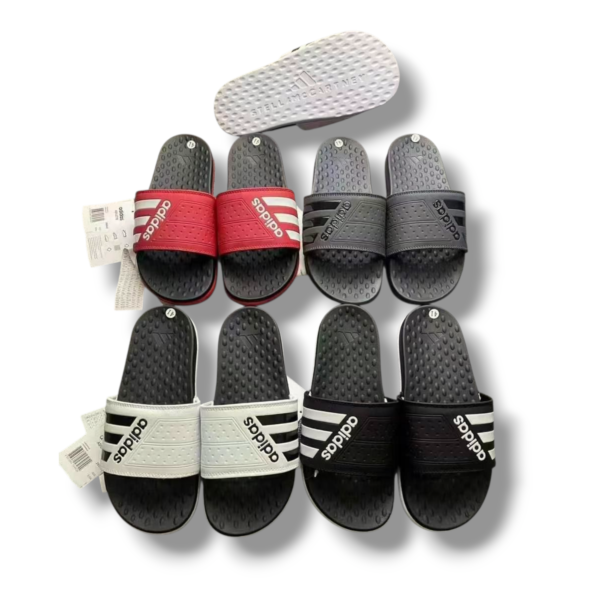 Row of Adidas slide sandals in white, red, gray and black with textured soles.
