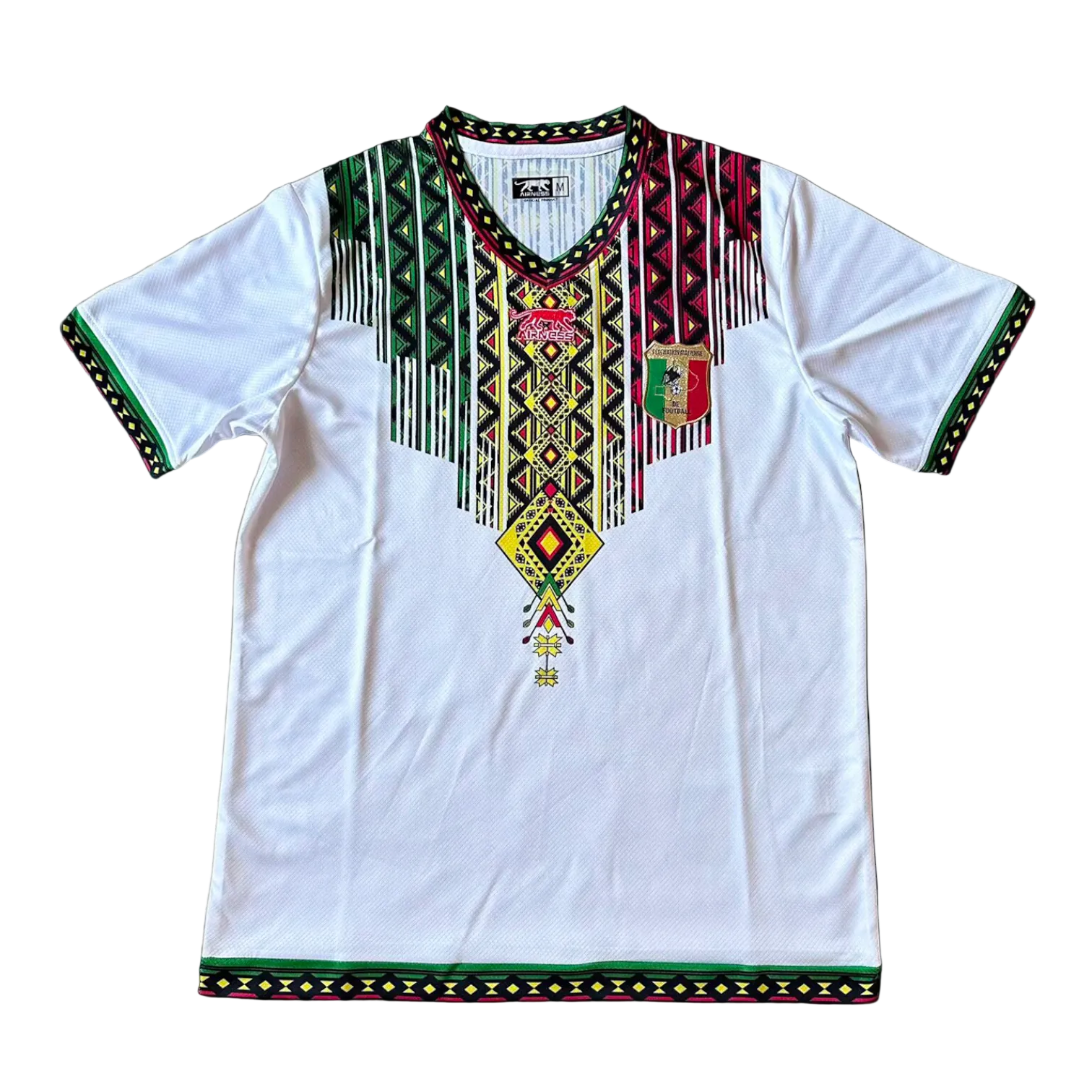 rn-image_picker_lib_temp_872b9652-7cd8-4d01-a6c8-7dc04e32fd49 White dashiki-style tunic with multicolor geometric embroidery around the V-neck and sleeves, white body, and a shield emblem on the left chest.