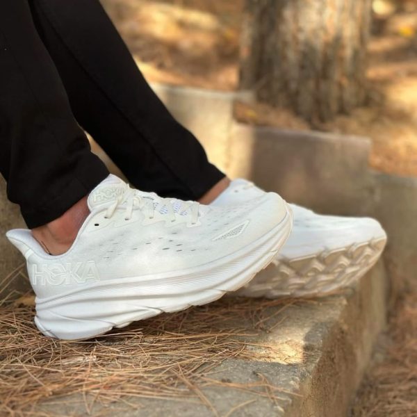 Person wearing white HOKA running shoes stepping down concrete steps outdoors with pine needles on the ground