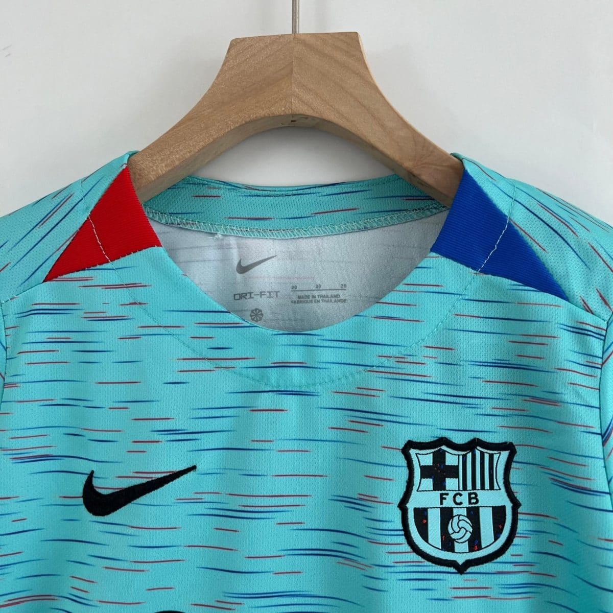 Close-up of a turquoise sports jersey on a wooden hanger, showing a Nike swoosh and a shield-shaped club badge.