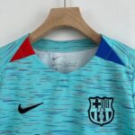 Close-up of a turquoise sports jersey on a wooden hanger, showing a Nike swoosh and a shield-shaped club badge.