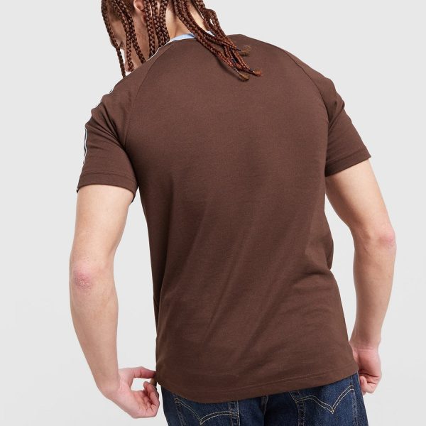 Back view of a man wearing a brown short-sleeve T-shirt and blue jeans, with long brown cornrow braids visible from behind.