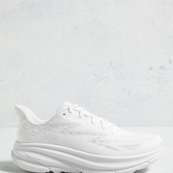 White Hoka running shoe with a chunky sole, set against a light blue textured background.
