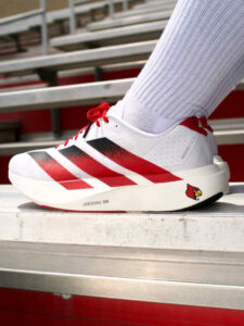 rn-image_picker_lib_temp_980766e8-04c9-4164-86d7-0e2eb6fb2644 | UAE SPORT STORE White athletic shoe with red stripes on metal bleachers; shows 'LIGHTSTRIKE PRO' on the midsole and a Cardinal logo on the heel.