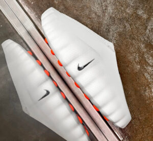 Pair of white soccer cleats with orange studs, shown from above, featuring a black Nike swoosh on each.