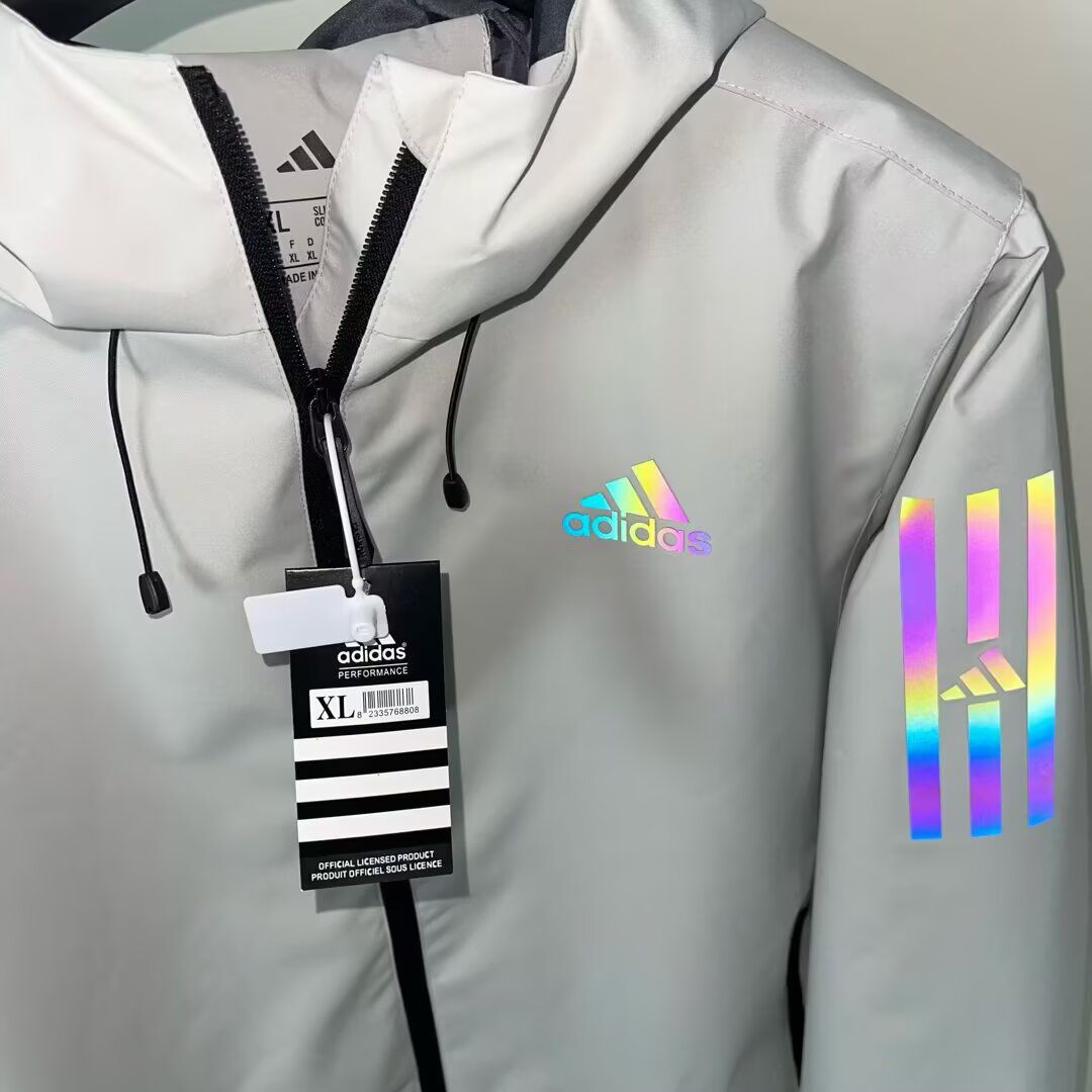 rn-image_picker_lib_temp_a1f03c81-1bd9-47d4-ad0b-e803c1afdc68 | UAE SPORT STORE Light gray Adidas windbreaker with a holographic rainbow logo on the chest and reflective rainbow stripes on the sleeve; size XL tag visible.