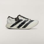 Close-up of a white Adidas sneaker with black stripes on a light background, showcasing the side and laces.