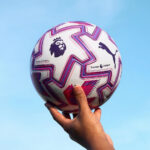 rn-image_picker_lib_temp_a4c064f3-7e05-43c0-bc34-f9de1802222b | UAE SPORT STORE A hand holding a white Premier League soccer ball against a clear blue sky.