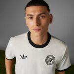 rn-image_picker_lib_temp_a50ebcc3-d44c-4f99-99b9-4bd73e4677a1 | UAE SPORT STORE Close-up of a person wearing a white jersey with black collar, showing Adidas logo and a circular club crest.