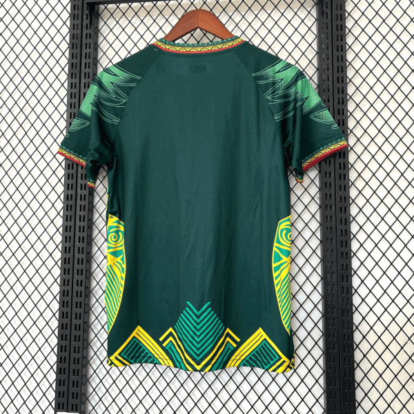 Back view of a dark green dress with bright yellow and turquoise geometric patterns along the hem and sides, hanging on a wooden hanger against a metal grid backdrop.