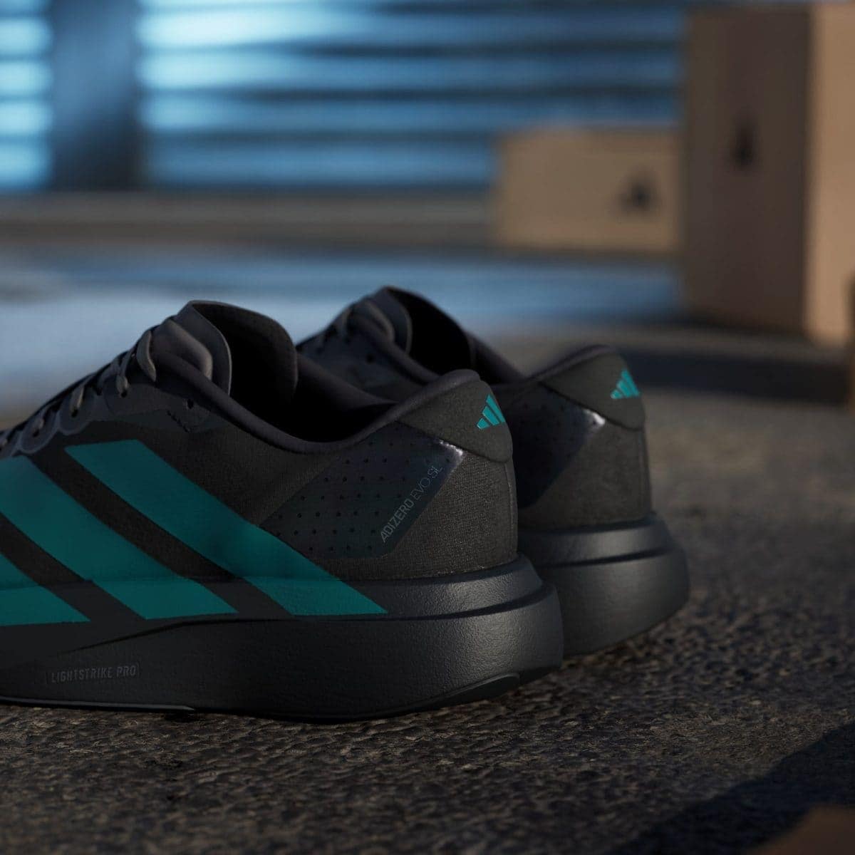 Close-up of black athletic sneakers with teal accents resting on a textured floor, blurred blue garage door in the background.