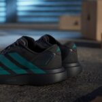 Close-up of black athletic sneakers with teal accents resting on a textured floor, blurred blue garage door in the background.