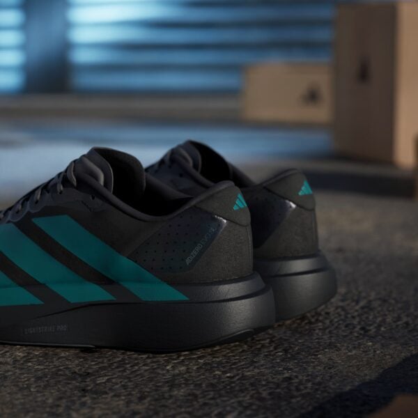 Close-up of black athletic sneakers with teal accents resting on a textured floor, blurred blue garage door in the background.