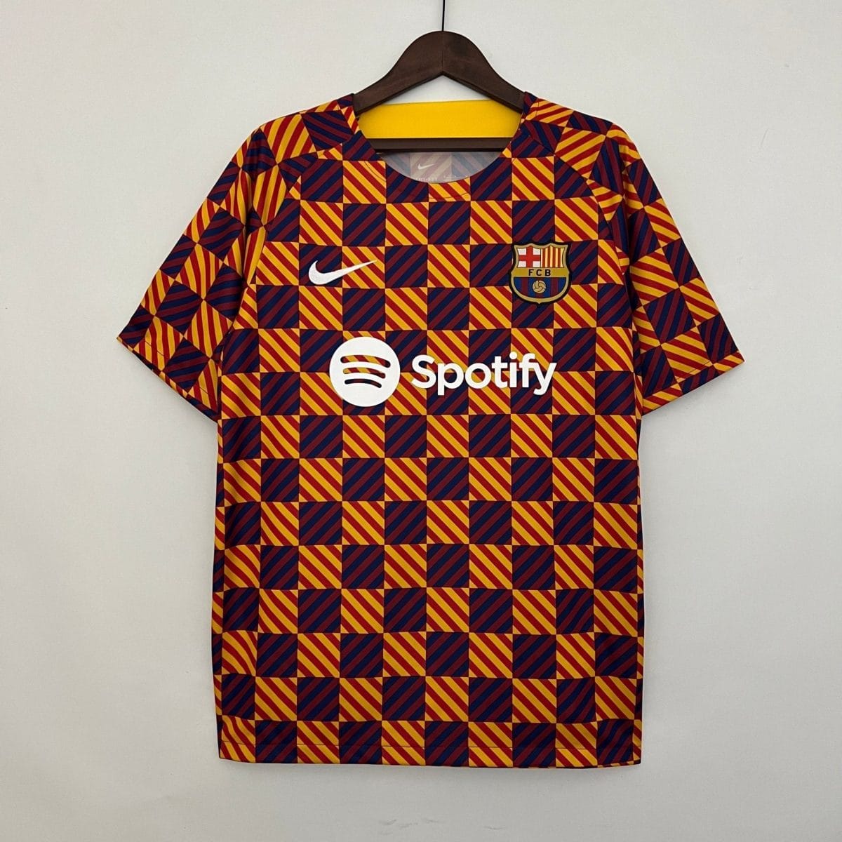 FC Barcelona football jersey on a hanger, featuring a red and yellow diagonal-square pattern with the club crest and white Nike swoosh.